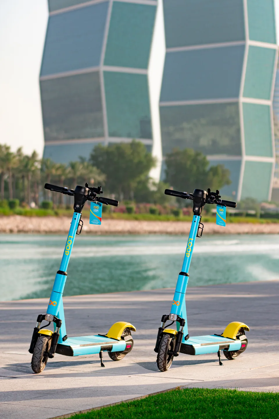 Blue and yellow Loop scooters parked by the water beside a tower in Qatar