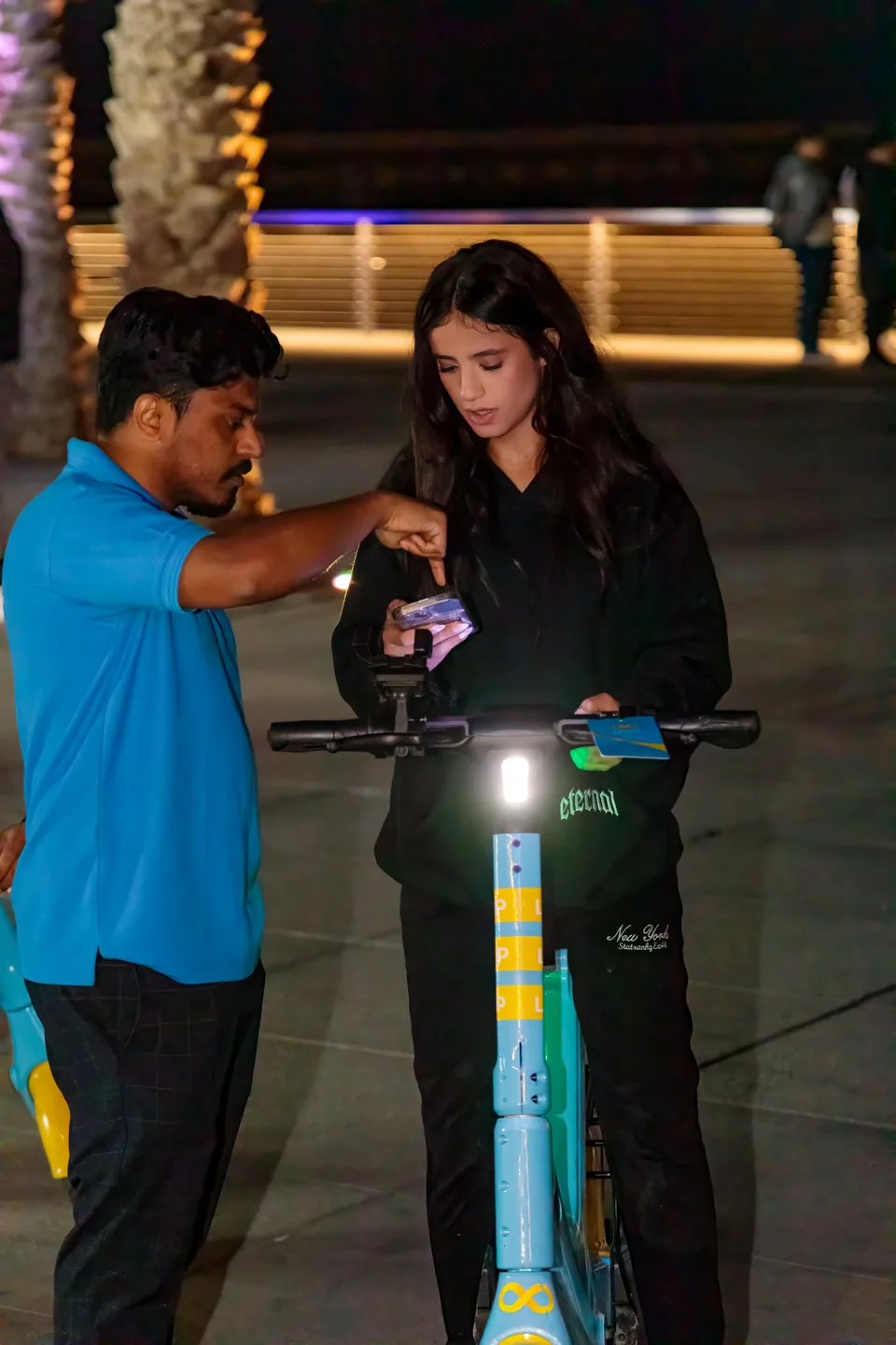 A man helping a woman with her phone beside a scooter