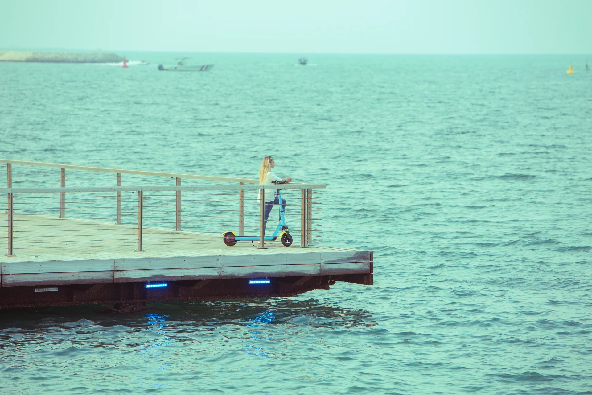 A woman with a parked Loop scooter on a waterfront boardwalk