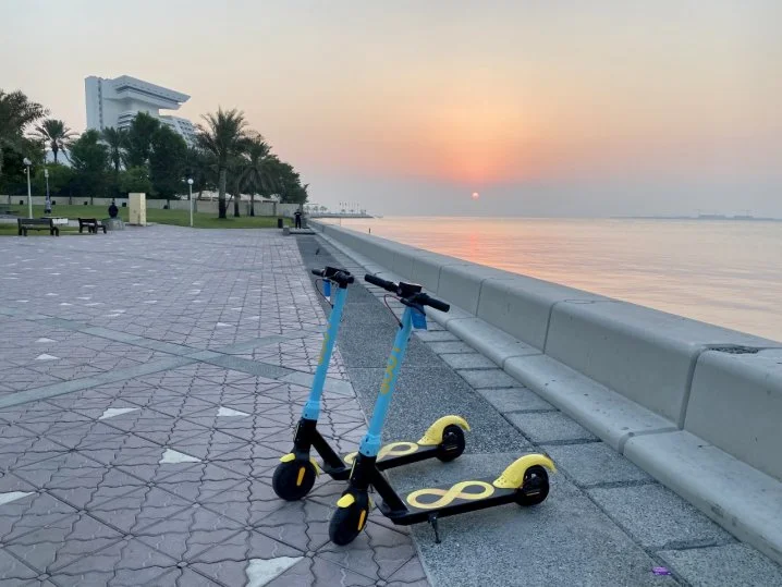 Two early Loop scooters parked beside the Corniche at sunset