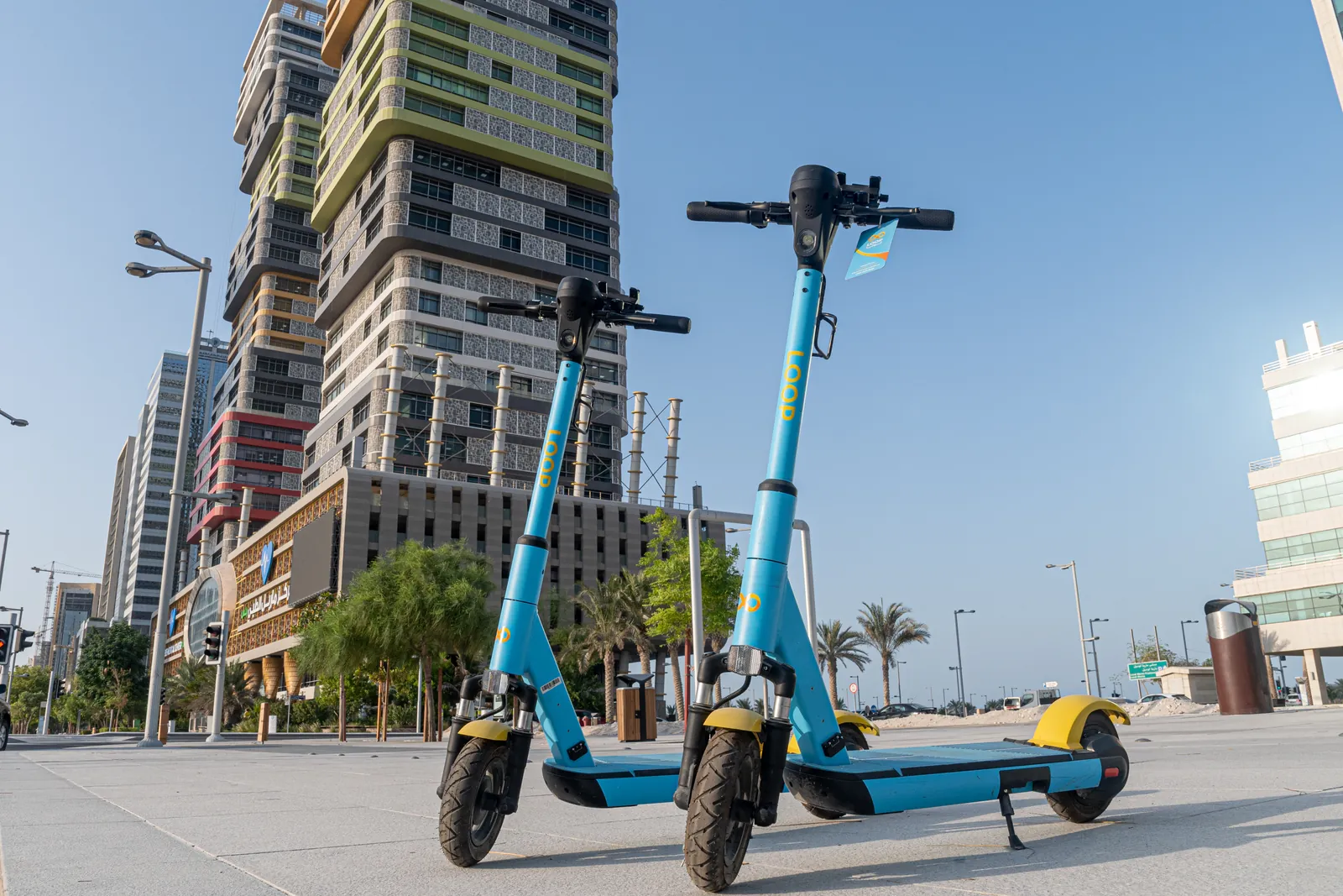 Two Loop scooters parked in a plaza beside city towers in Qatar