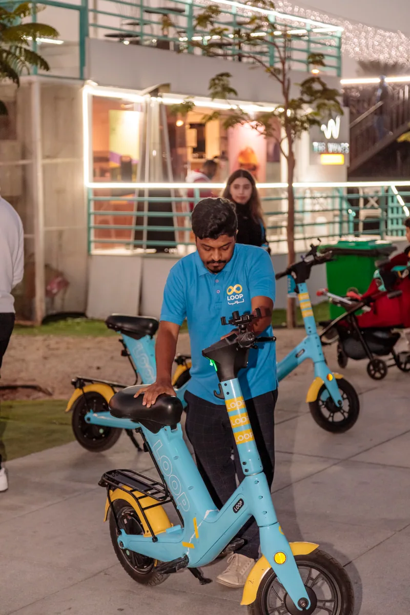 A man in a blue shirt looking over a parked scooter at an evening gathering