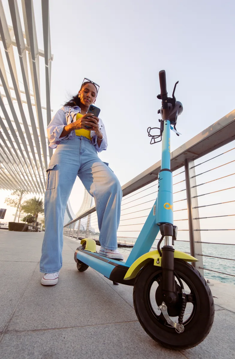 A woman using her phone beside a parked Loop scooter