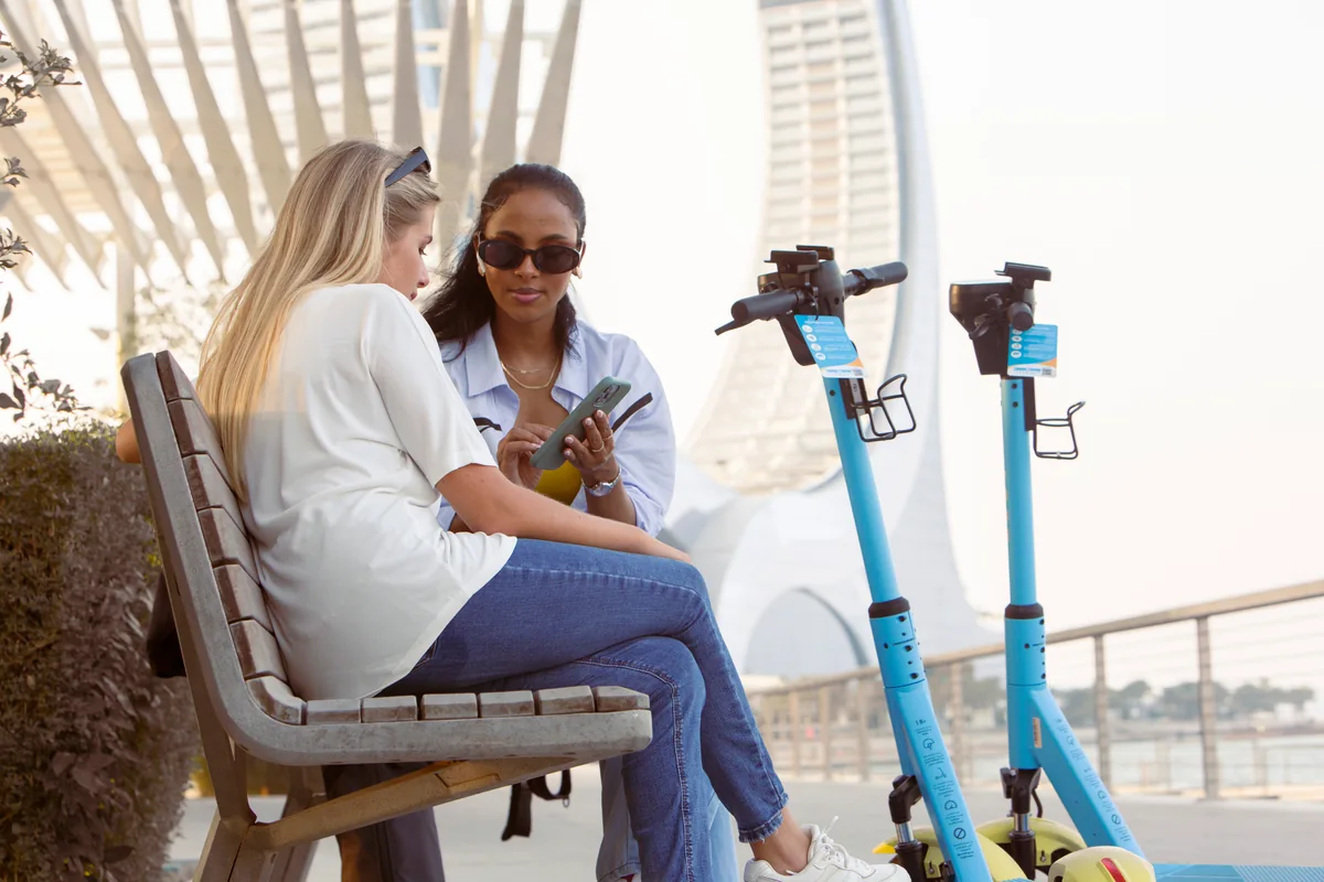 Two women seated checking a phone beside stationary Loop scooters