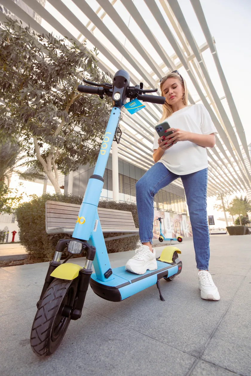 A rider checking her phone beside a stationary Loop scooter